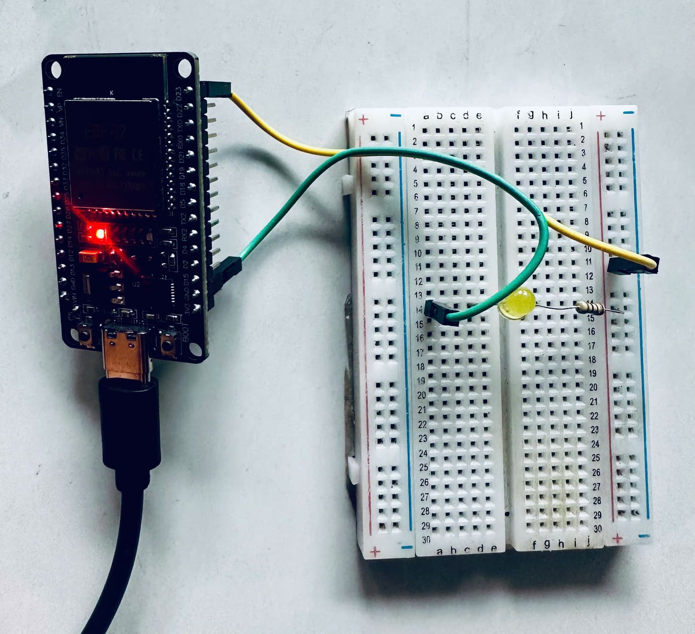Ảnh chụp mạch thật: bo ESP32 DevKit cắm cáp USB, hai dây nối sang breadboard có LED vàng và điện trở.